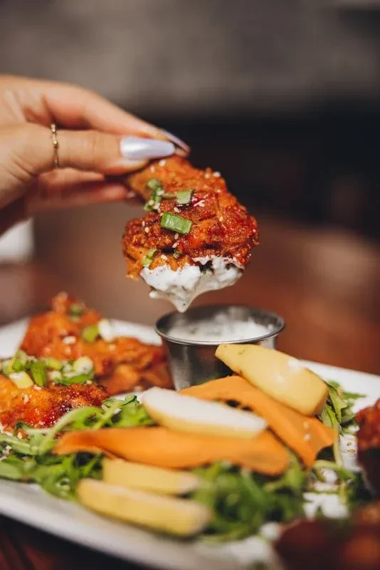 Hand dips crispy fried chicken with sesame into creamy white sauce.