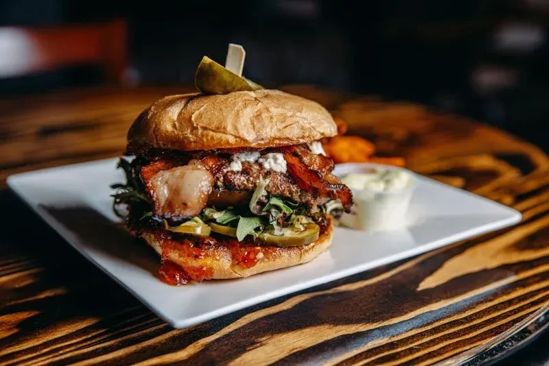 Gourmet burger with bacon, melted cheese, jalapeños, pickle, and fries.