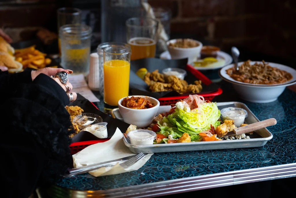 Diner table with wedge salad, chili, fried items, drinks, and a hand.