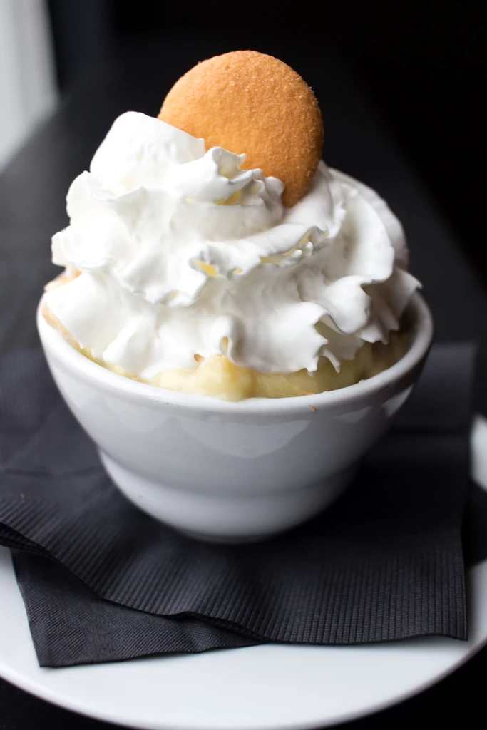 Banana pudding in a white bowl, topped with whipped cream and a wafer.