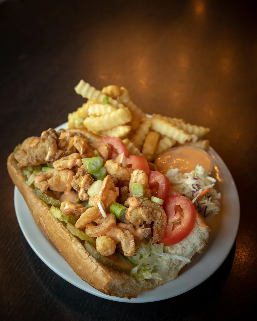 Overflowing fried seafood po'boy with crinkle fries and coleslaw meal.