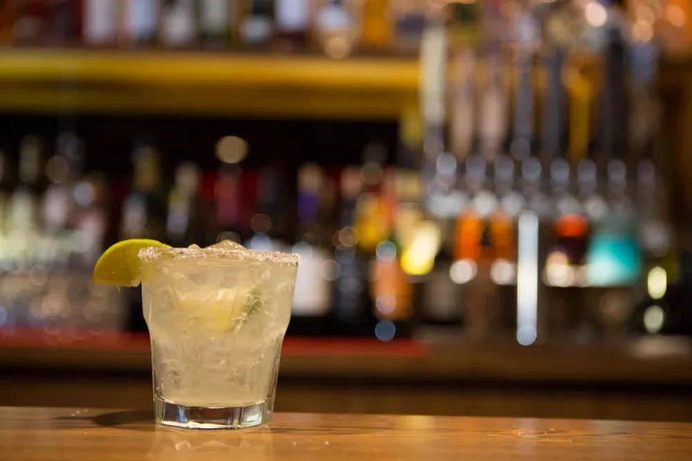 Margarita with lime, salted rim, on a wooden bar counter.