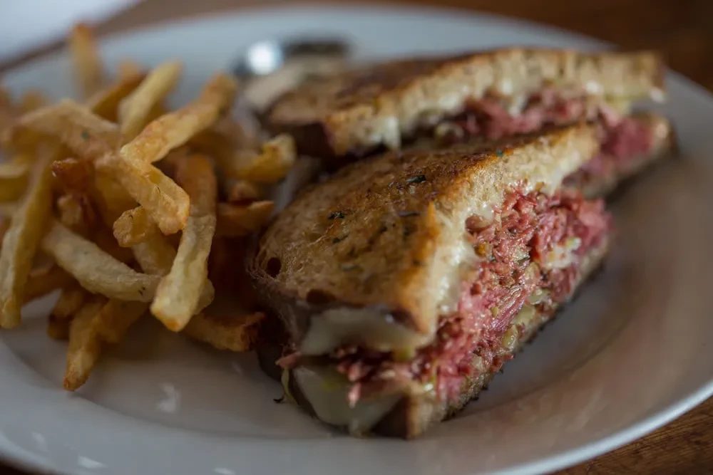 Grilled deli sandwich halves and golden french fries on a white plate.