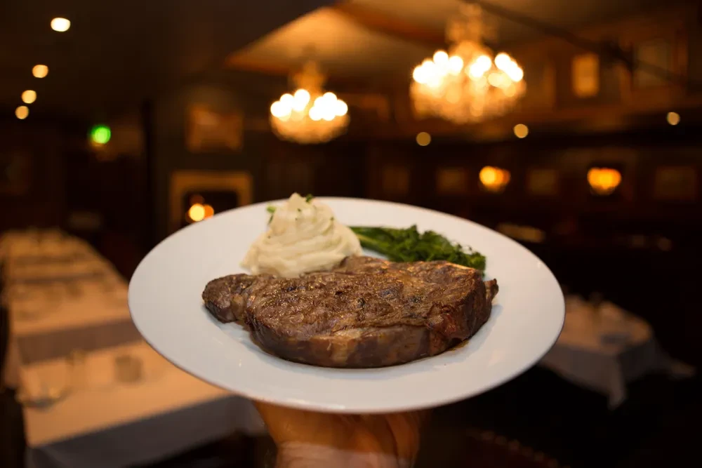 Hand holds plate with grilled steak, mashed potatoes, and green vegetables.