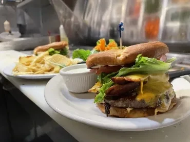 Two plates with double bacon cheeseburgers, fries, and dipping sauce.