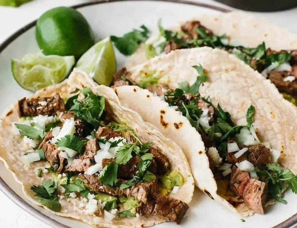 Three street tacos filled with steak, avocado, cilantro, and lime.