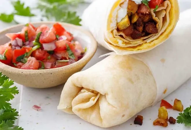 Two burritos, one open with egg, meat, and potatoes, next to fresh salsa.