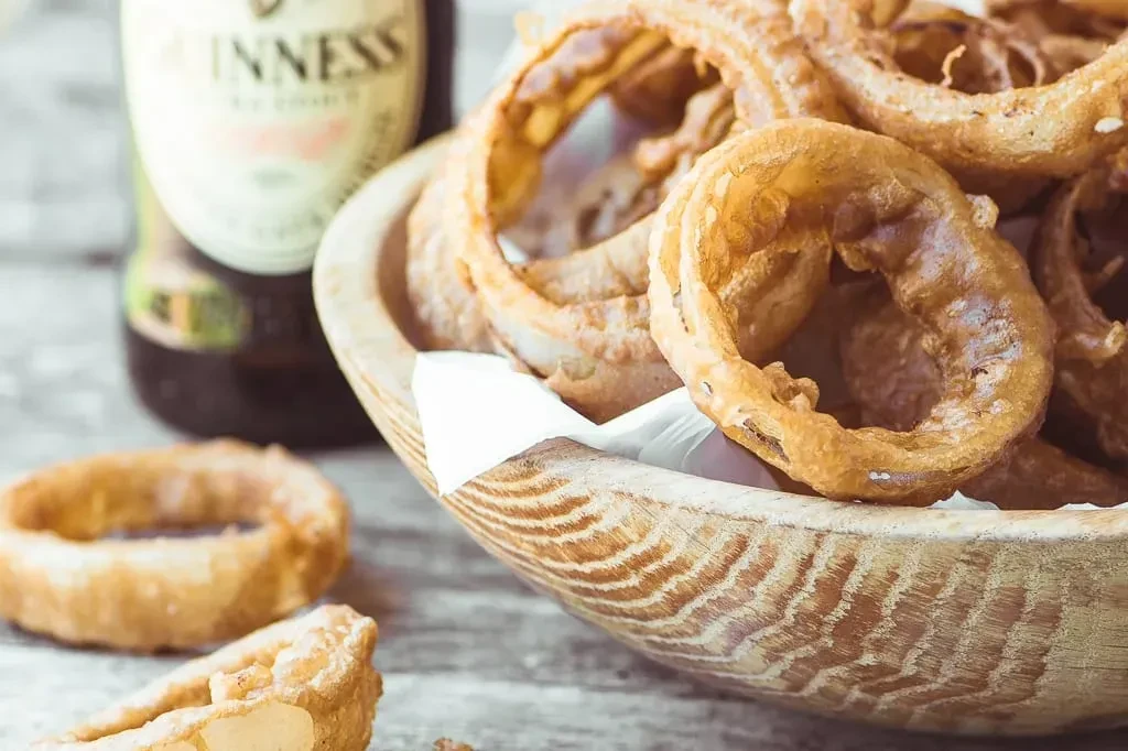 Crispy onion rings spilling from a wooden bowl, with Guinness beer.