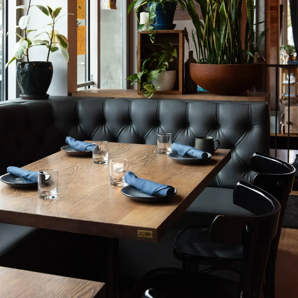 Modern restaurant dining area with set table, dark booth, and plants.