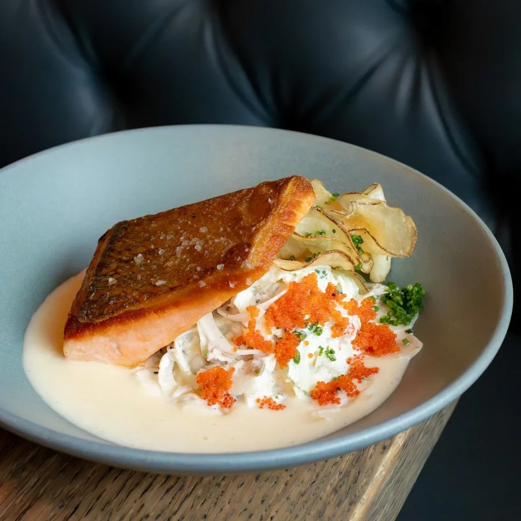 Meticulously plated salmon with crispy skin, roe, herbs, and salad.