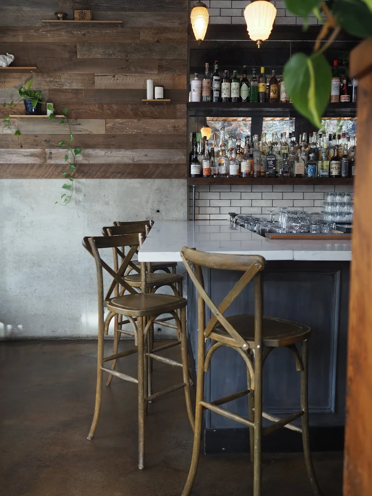 Modern rustic bar interior with counter, stools, liquor, and wooden wall.