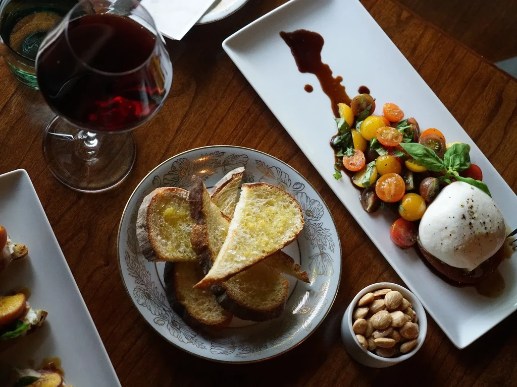 Overhead: burrata caprese, toasted bread, almonds, red wine on wooden table.