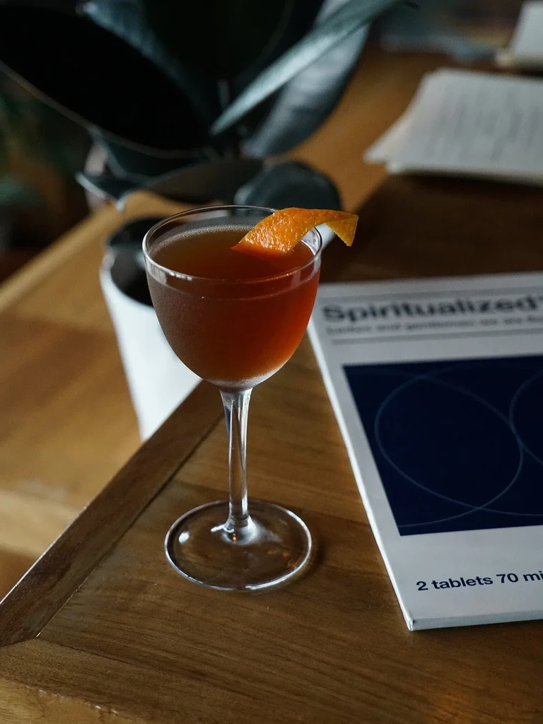 Chilled amber cocktail with orange peel in coupe glass on wood.