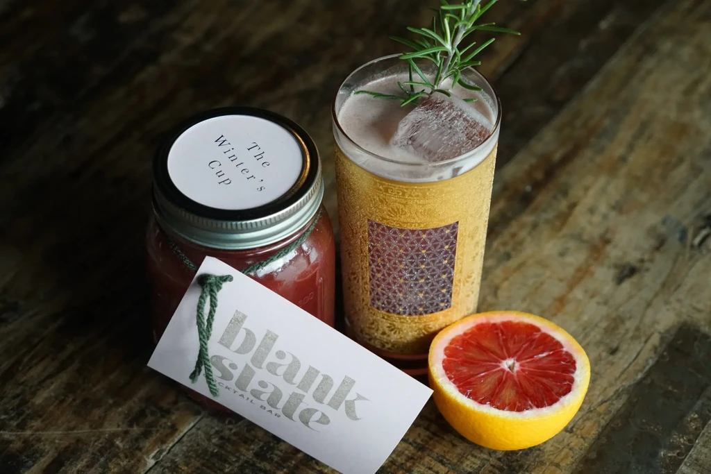 Two craft cocktails with blood orange and rosemary on a wooden surface.