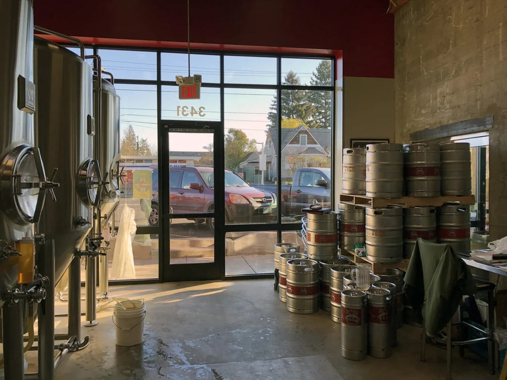 Brewery interior with two steel fermentation tanks and stacked kegs.