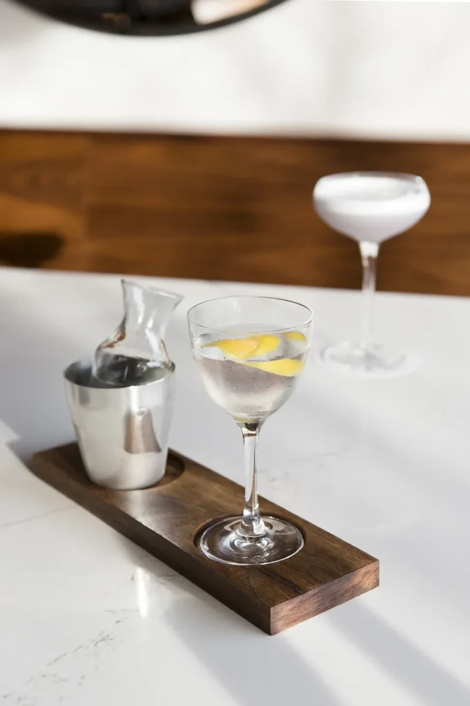 Clear cocktail with lemon, milky drink, and decanter on marble.