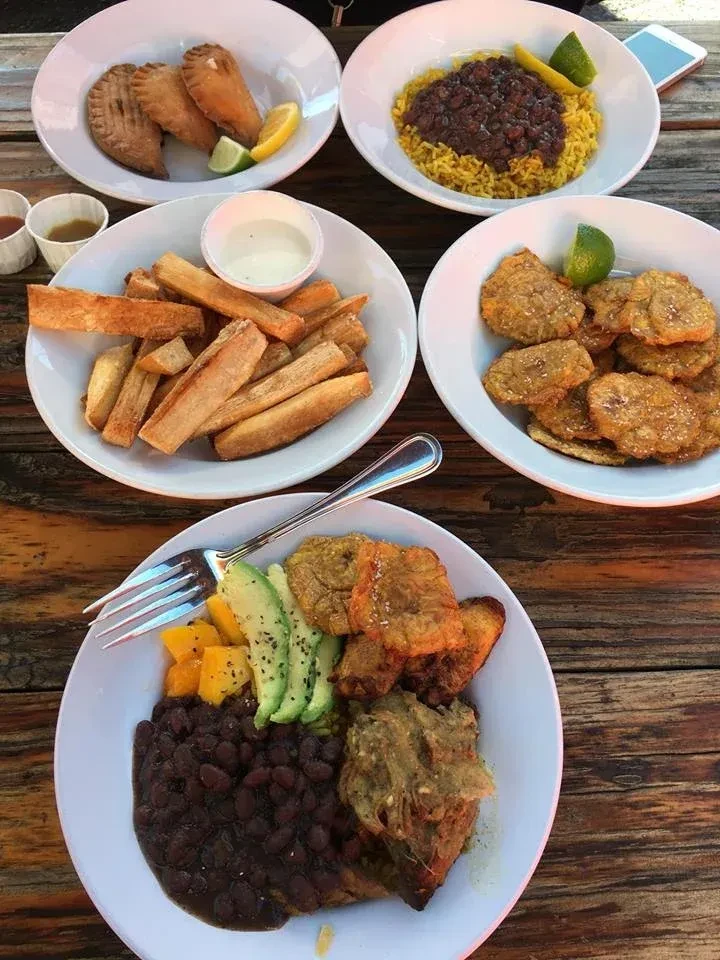 Five plates of diverse Latin American food on a rustic wooden table.