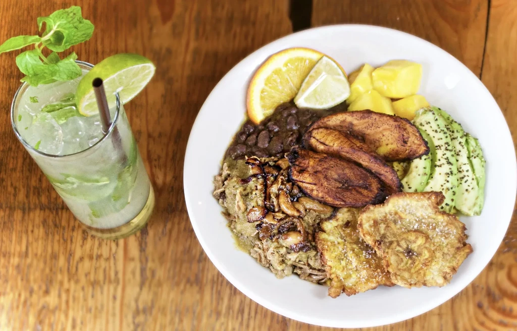 Colorful meal bowl with plantains, avocado, and mojito on a rustic table.
