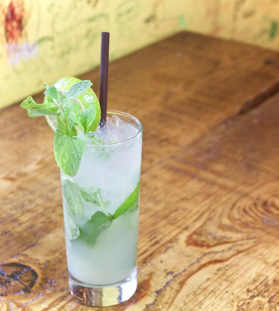 Mint-lime iced drink in glass with straw on a wooden table.
