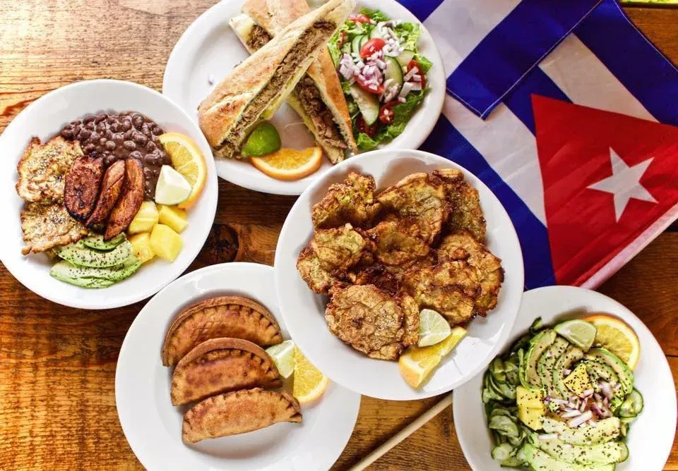 Overhead view of diverse Cuban food on a rustic table with flag.