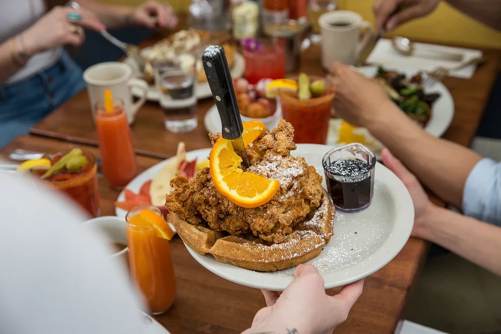Fried chicken and waffles served with syrup at a busy restaurant table.