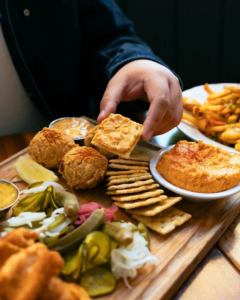 Hand holding cracker with dip from a rustic platter.