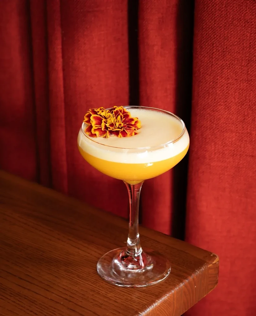 Golden and white layered cocktail in coupe glass, garnished with a flower.