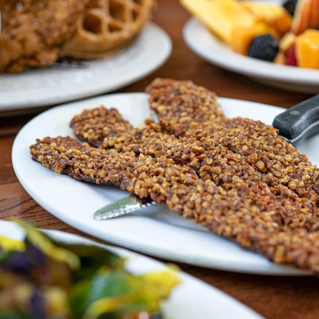 Close-up of nut-crusted strips, waffle, and fruit salad on a table.