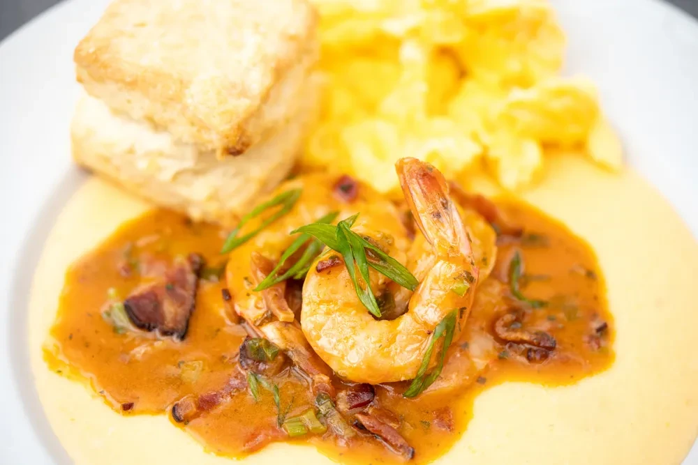 Close-up of shrimp and grits, biscuits, and blurred scrambled eggs.