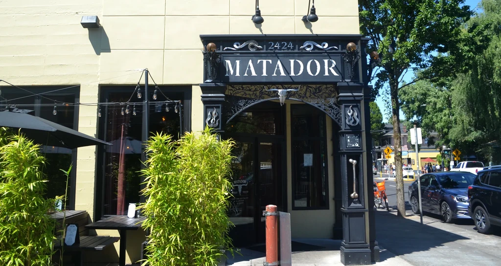Dark, ornate "MATADOR" restaurant entrance with bull skull, city street.