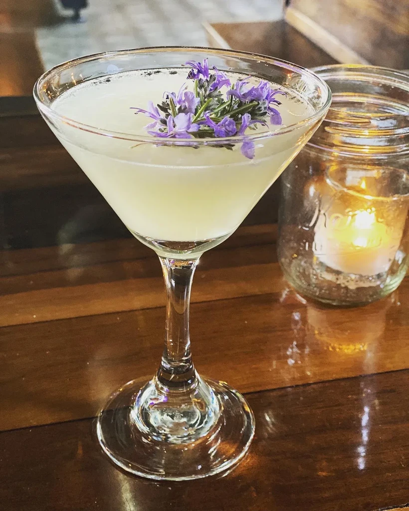 Martini cocktail with lavender on wood, soft light from a candle.