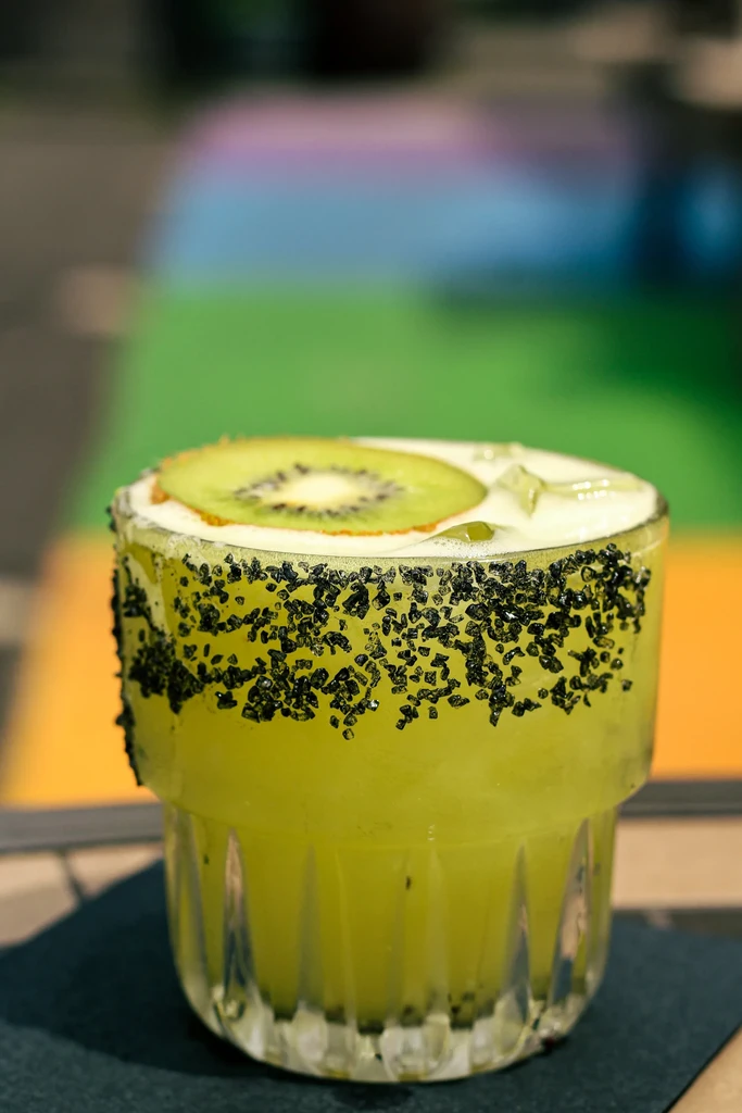 Green-yellow cocktail in textured glass, dark sugar rim, kiwi slice.