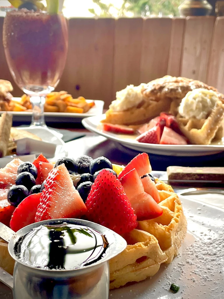 Close-up of a golden waffle with berries, powdered sugar, and syrup.