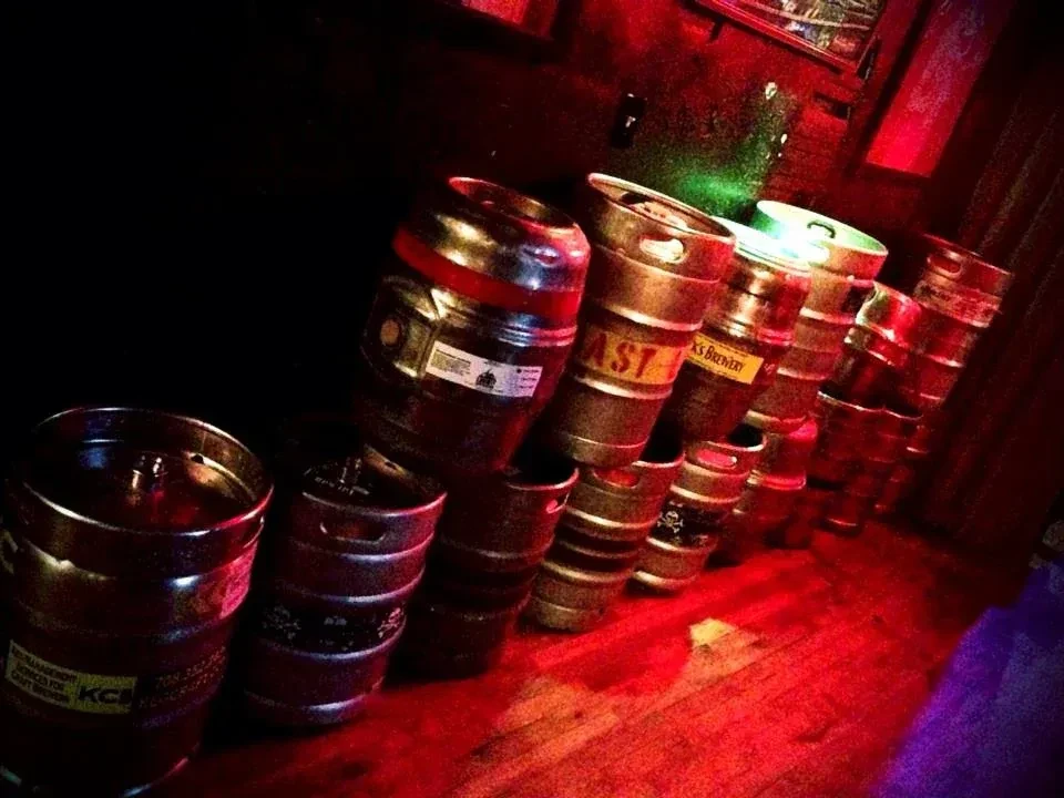 Stacked beer kegs glow under contrasting red and green lights.