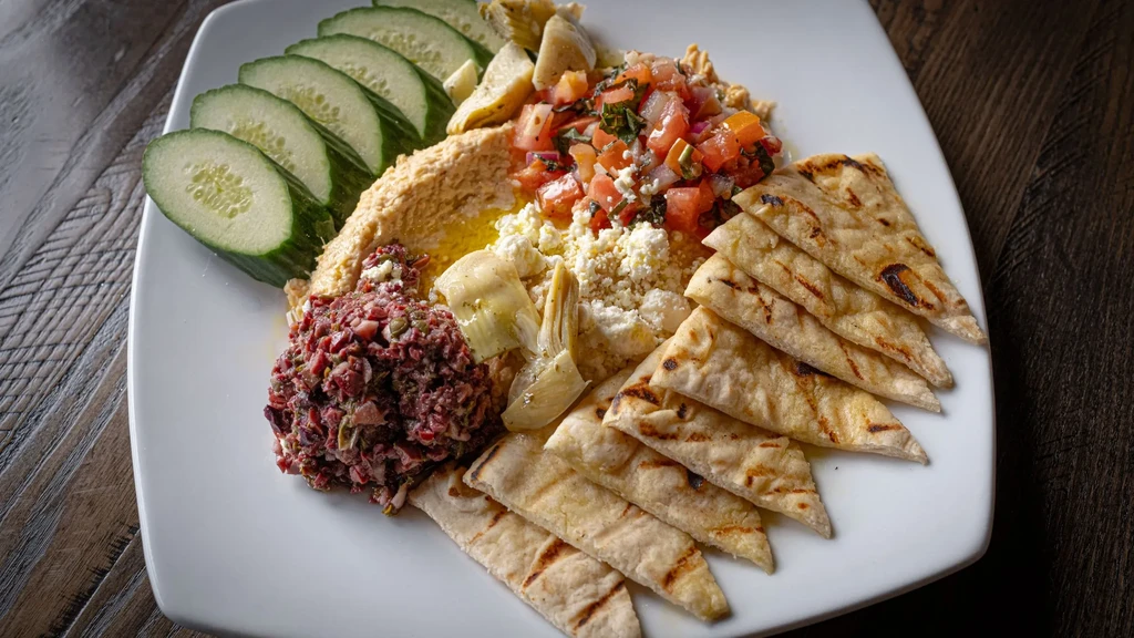Hummus platter with tomato, feta, olive spread, artichokes, cucumber, and pita.