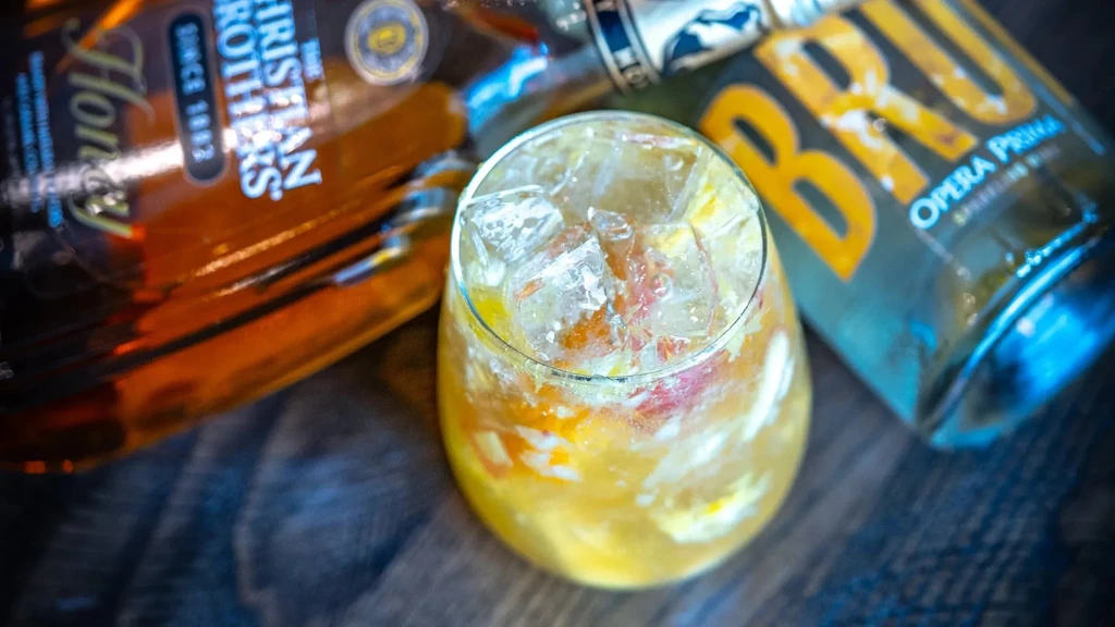 Close-up of a citrus cocktail on ice with blurred bottles in the background.