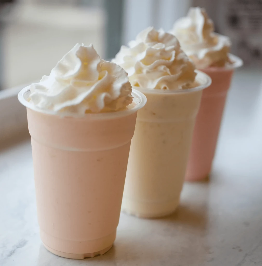 Three creamy milkshakes: pink, yellow, and pink, with whipped cream.