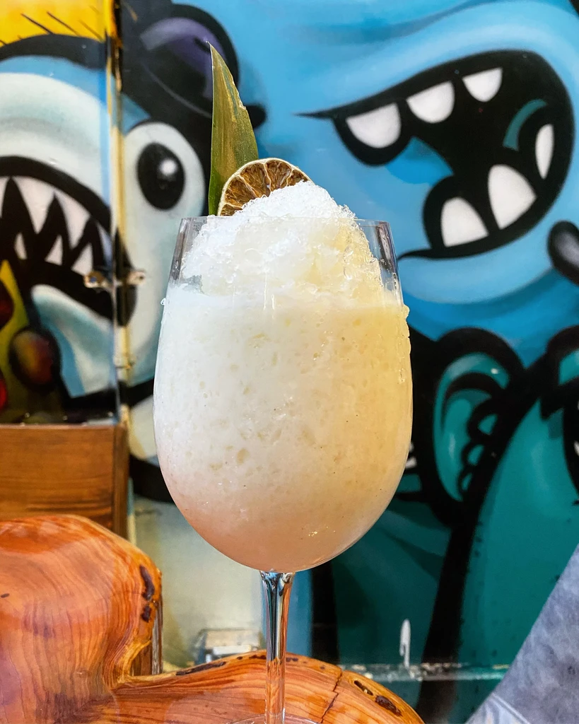 Creamy white frozen cocktail on wood before vibrant monster graffiti.