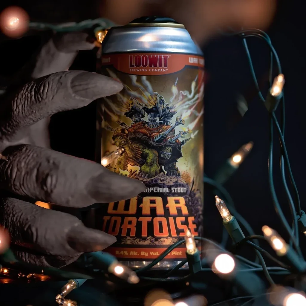 Gnarled monster hand holds War Tortoise stout can with string lights.