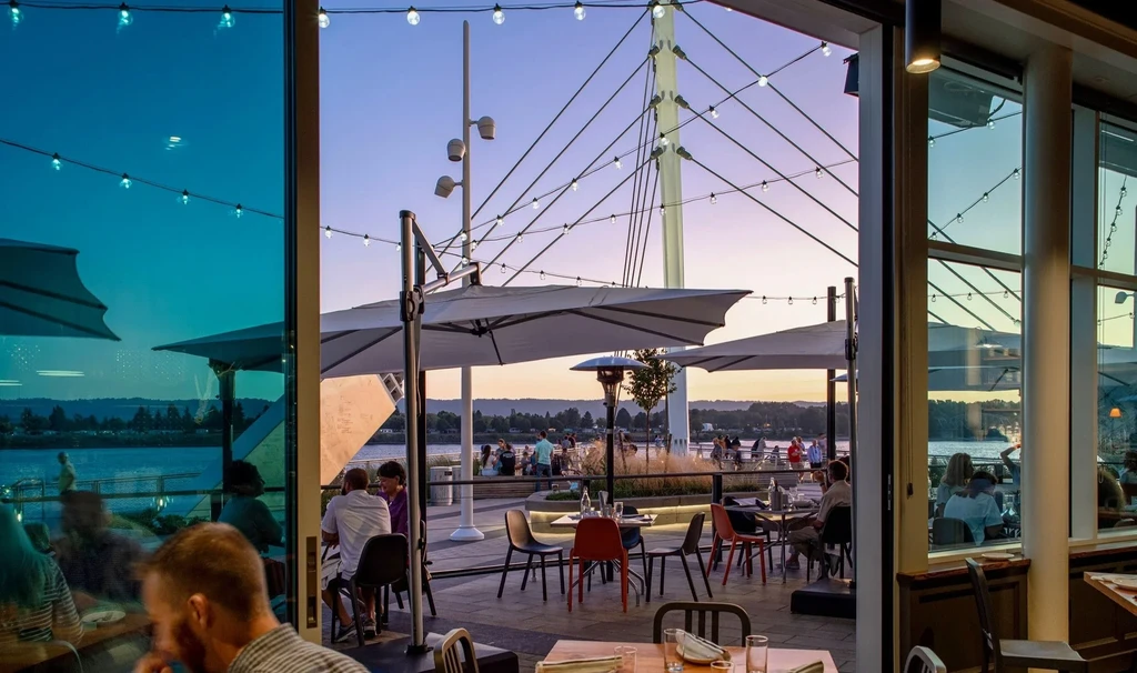 Vibrant evening on a restaurant patio overlooking a bridge and water.