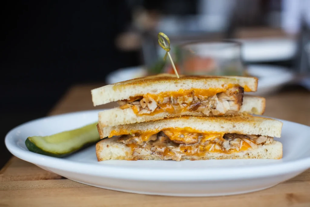 Grilled shredded meat and cheese sandwich with a dill pickle.