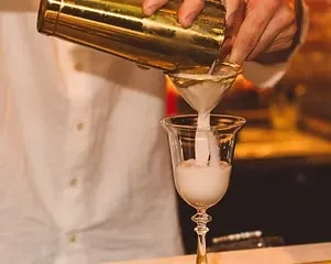 Bartender pouring white drink from shaker into an elegant glass.