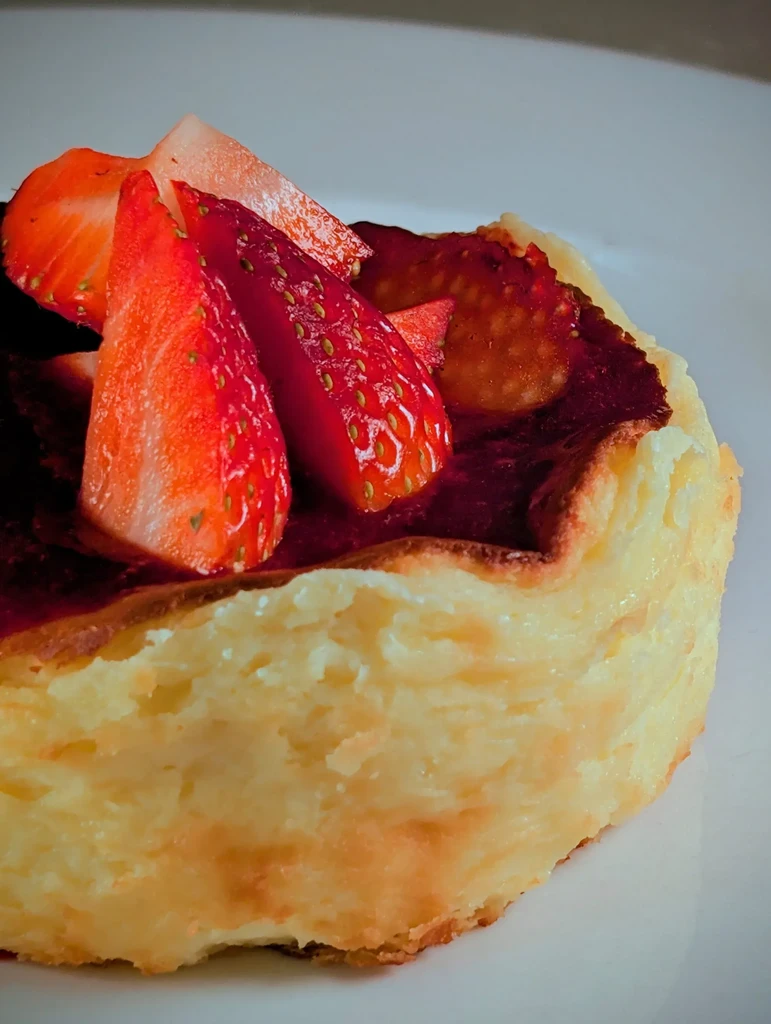 Pale yellow dessert with caramelized top, jam, and fresh strawberries.