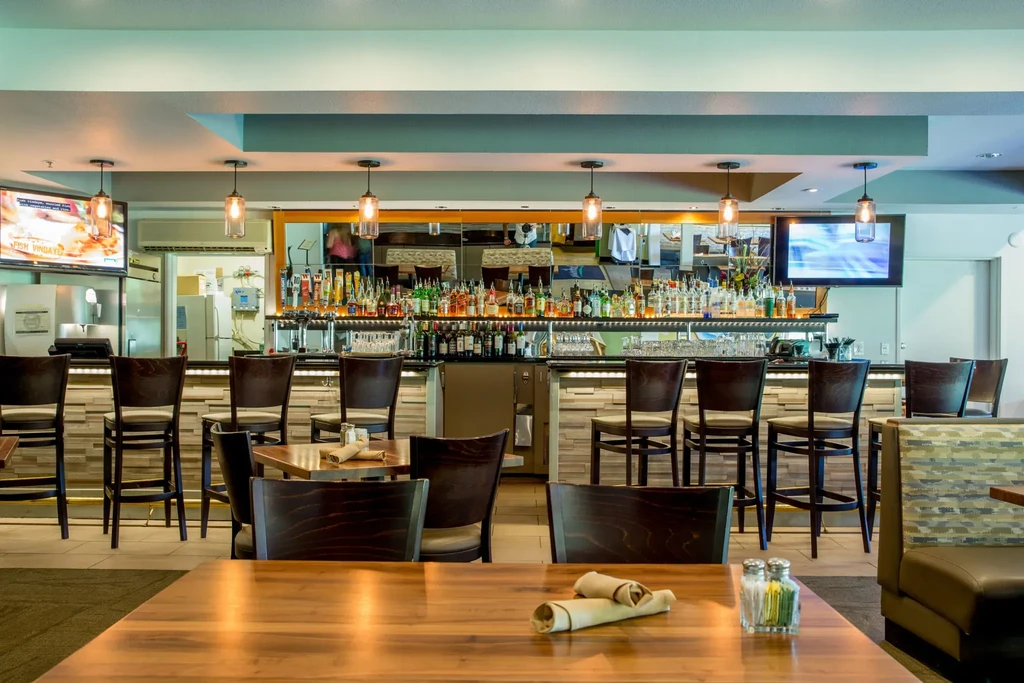 Modern restaurant bar with spirits, stools, televisions, and dining tables.