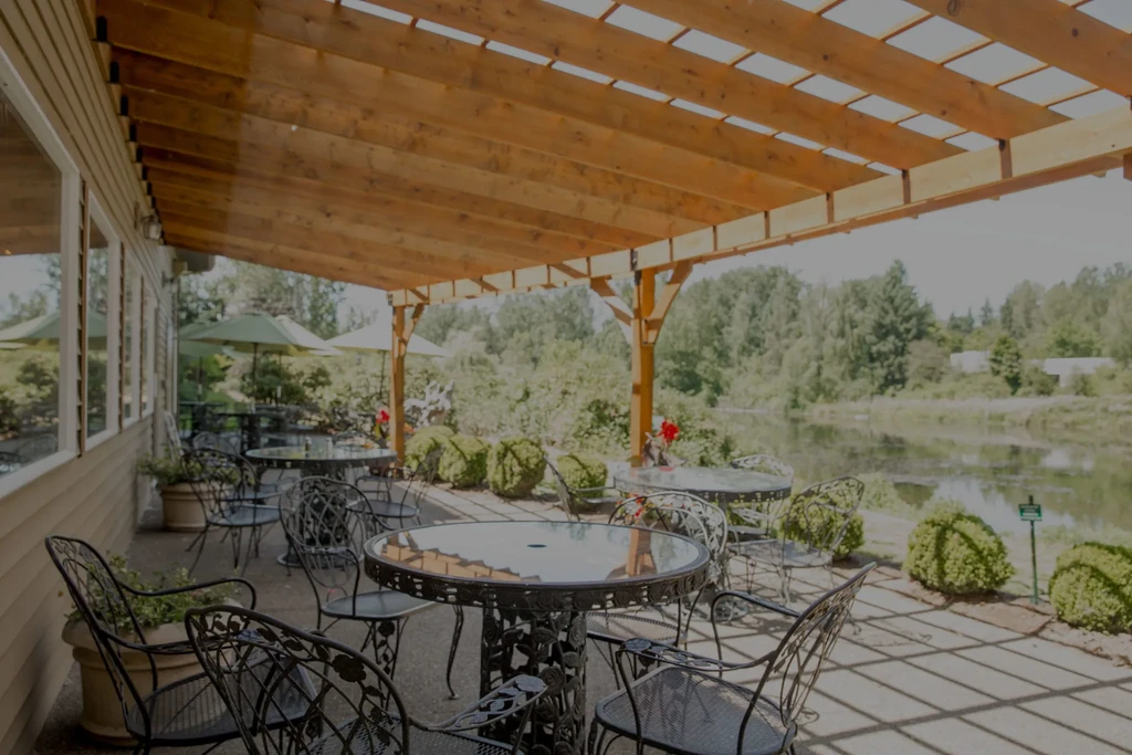 Empty outdoor patio with tables, pergola, lake, and trees.