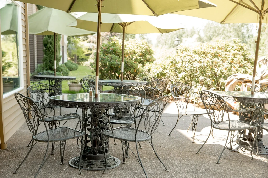 Restaurant patio with ornate wrought iron tables, chairs, and green umbrellas.