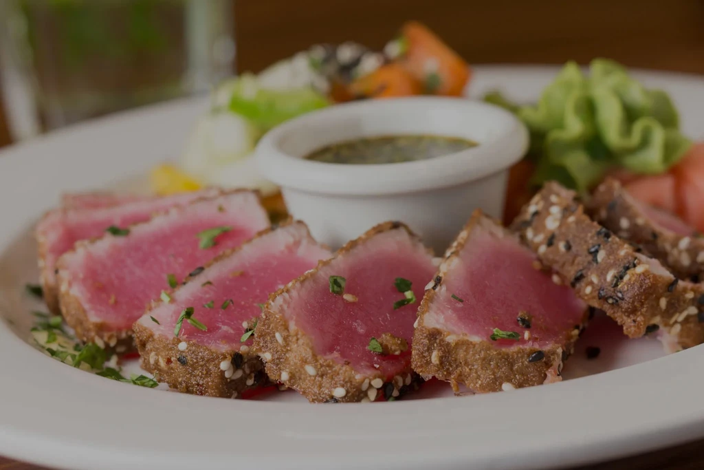 Medium-rare seared tuna with sesame crust, herbs, salad, and sauce.