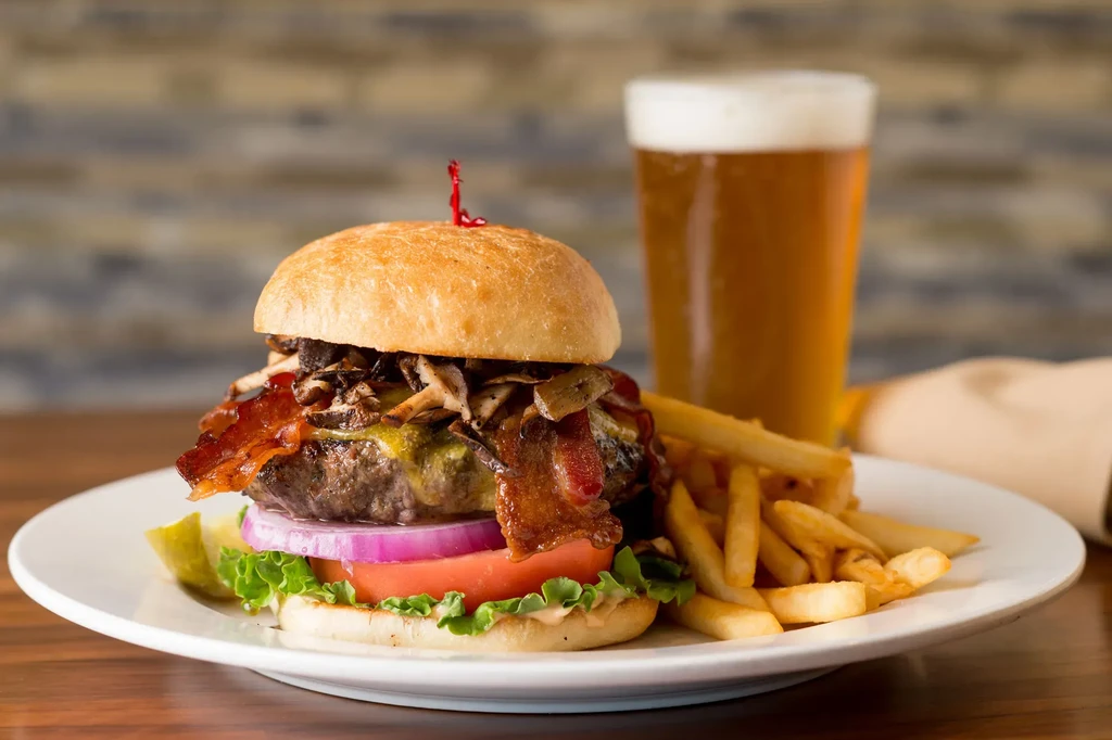 A stacked burger, golden fries, and a pint of amber beer.