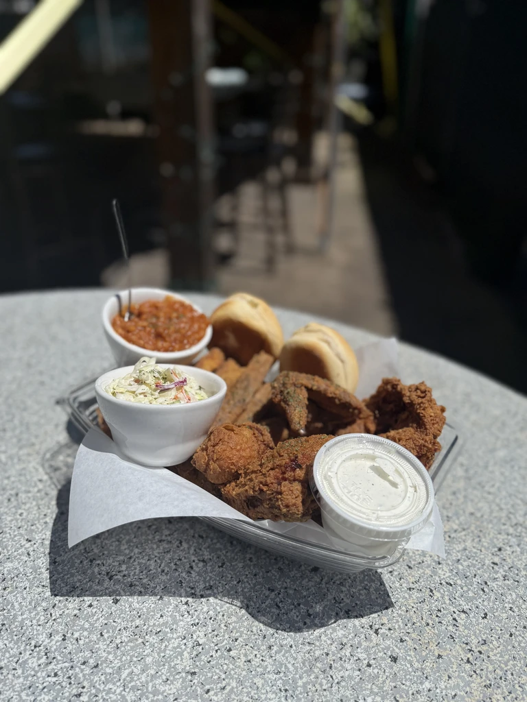 Tray of fried chicken, rolls, coleslaw, and sauces served outdoors.