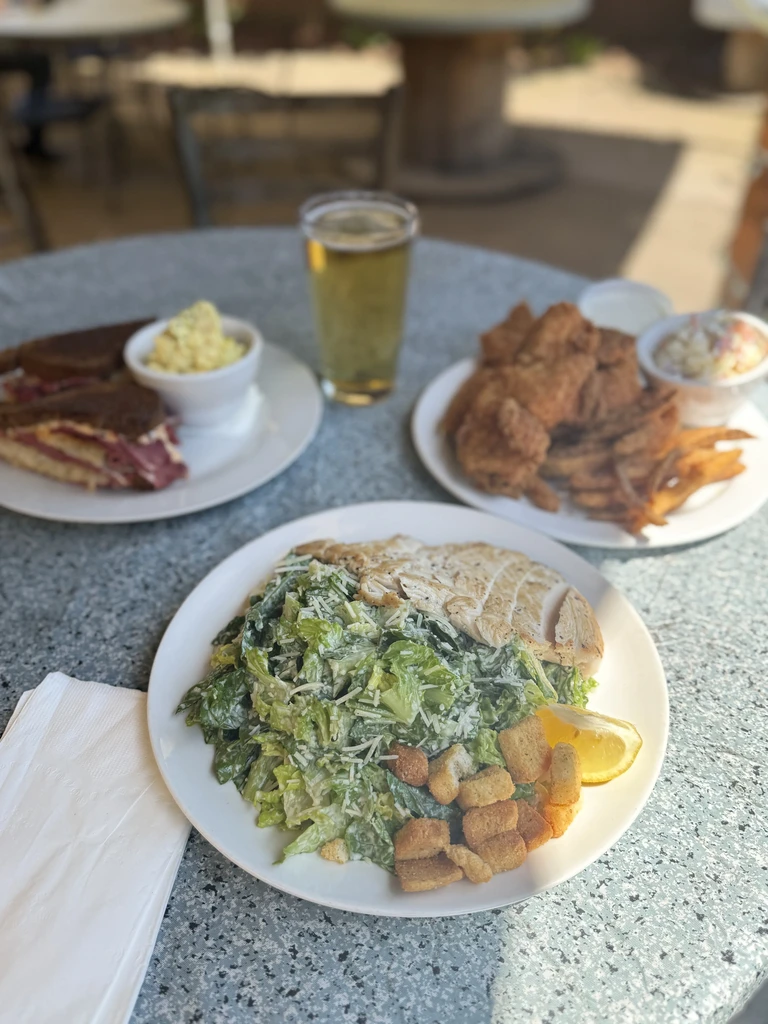Three full plates: Caesar salad, sandwich, fried food, and a beer.